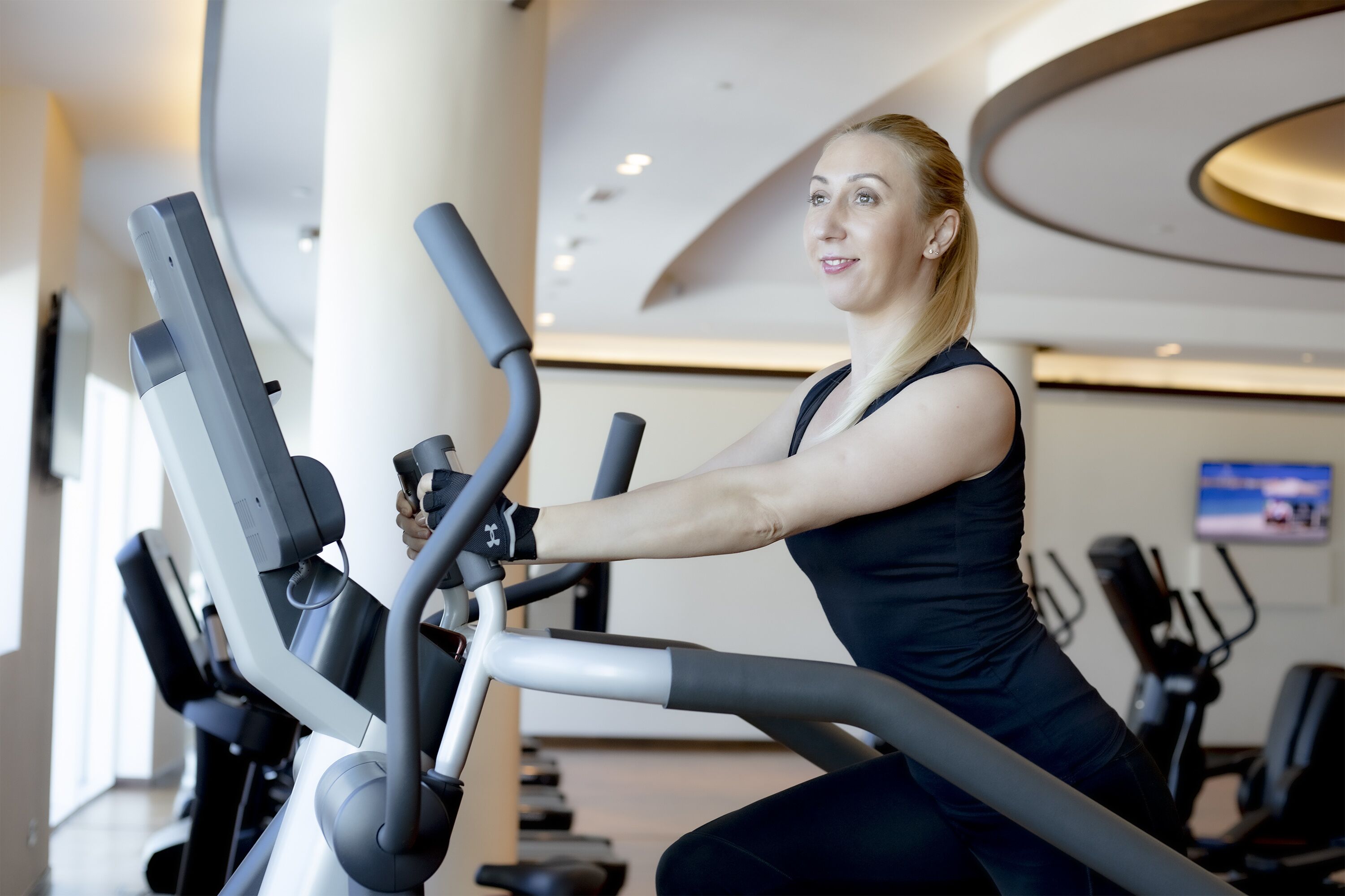 A woman using an elliptical machine in a gym with modern design and various exercise equipment.