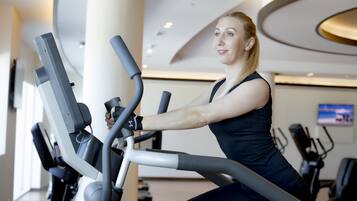 A woman using an elliptical machine in a gym with modern design and various exercise equipment.