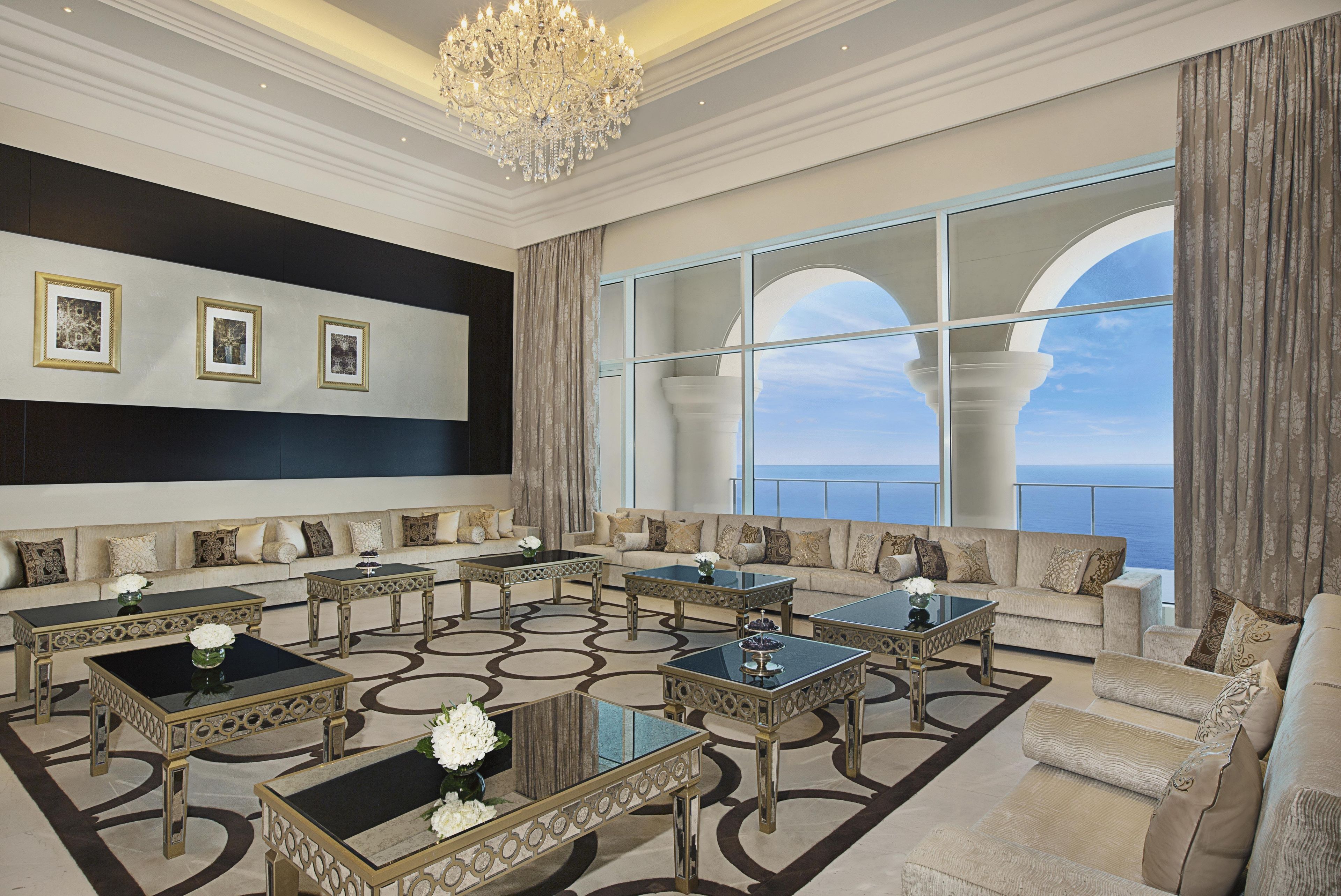A luxurious living room with a large window offering a view of the sea, elegant furniture, and a chandelier.