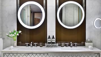 Un baño con dos lavamanos, un espejo grande con luces redondas, un florero y un detalle decorativo en los azulejos.