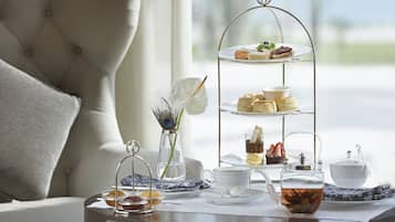 A three-tiered dessert stand with pastries and a teapot on a table in a room with a city view.
