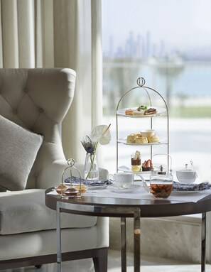 A three-tiered dessert stand with pastries and a teapot on a table in a room with a city view. - Waldorf Astoria Dubai Palm Jumeirah (Dubai)