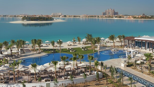 Un resort con una amplia piscina, palmeras y vistas a una isla distante y al horizonte de la ciudad.