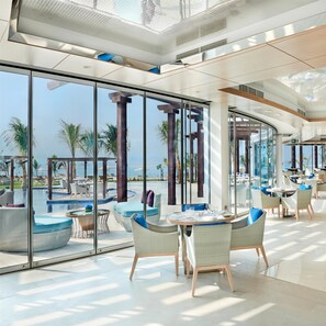 Un hall d’hôtel moderne avec de grandes baies vitrées, un espace piscine et des sièges en plein air.