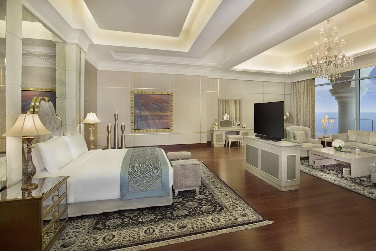 A spacious bedroom with a large bed, a television, a seating area with a sofa and armchairs, and a view of the ocean.