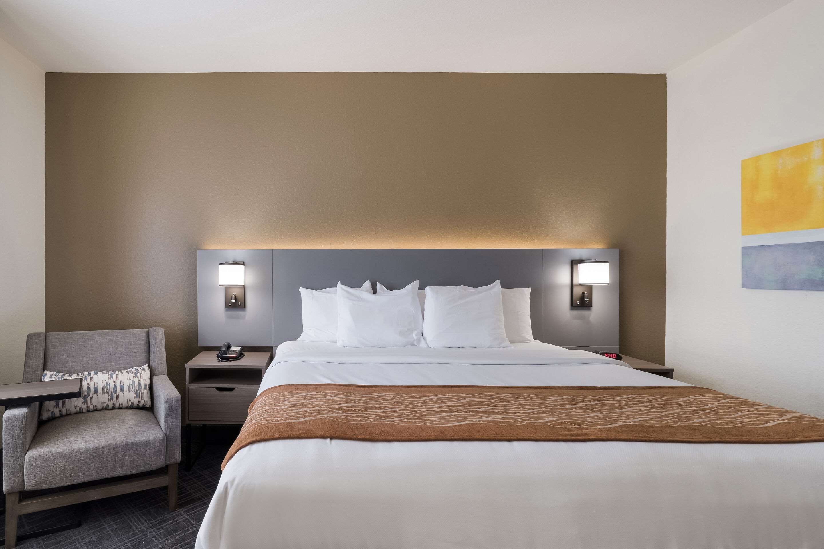 Une chambre d’hôtel avec un lit, une table de chevet, une chaise et une lampe fixée au mur.