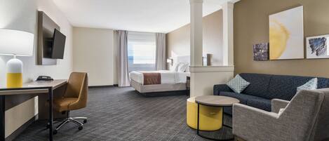 Une chambre d’hôtel comprenant un lit, un canapé, un bureau avec une chaise, un téléviseur fixé au mur et des œuvres d’art accrochées aux murs.