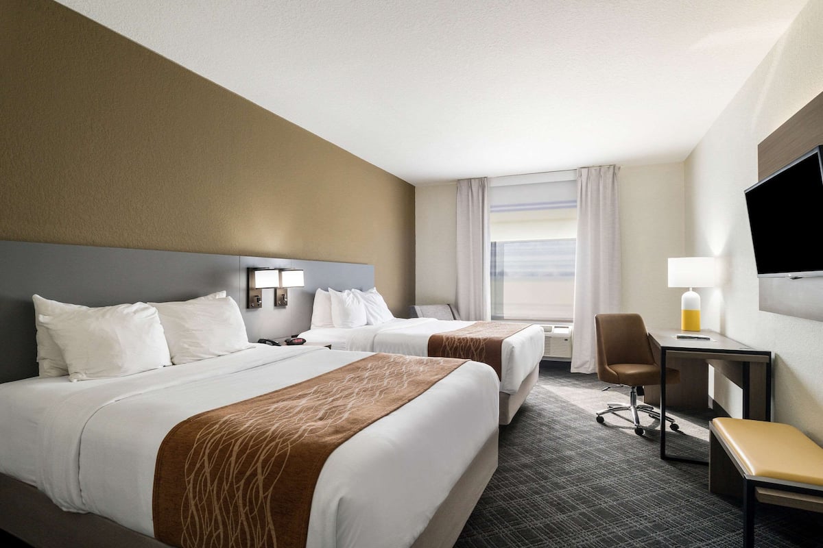 A hotel room with two beds, a desk, a chair, and a TV.