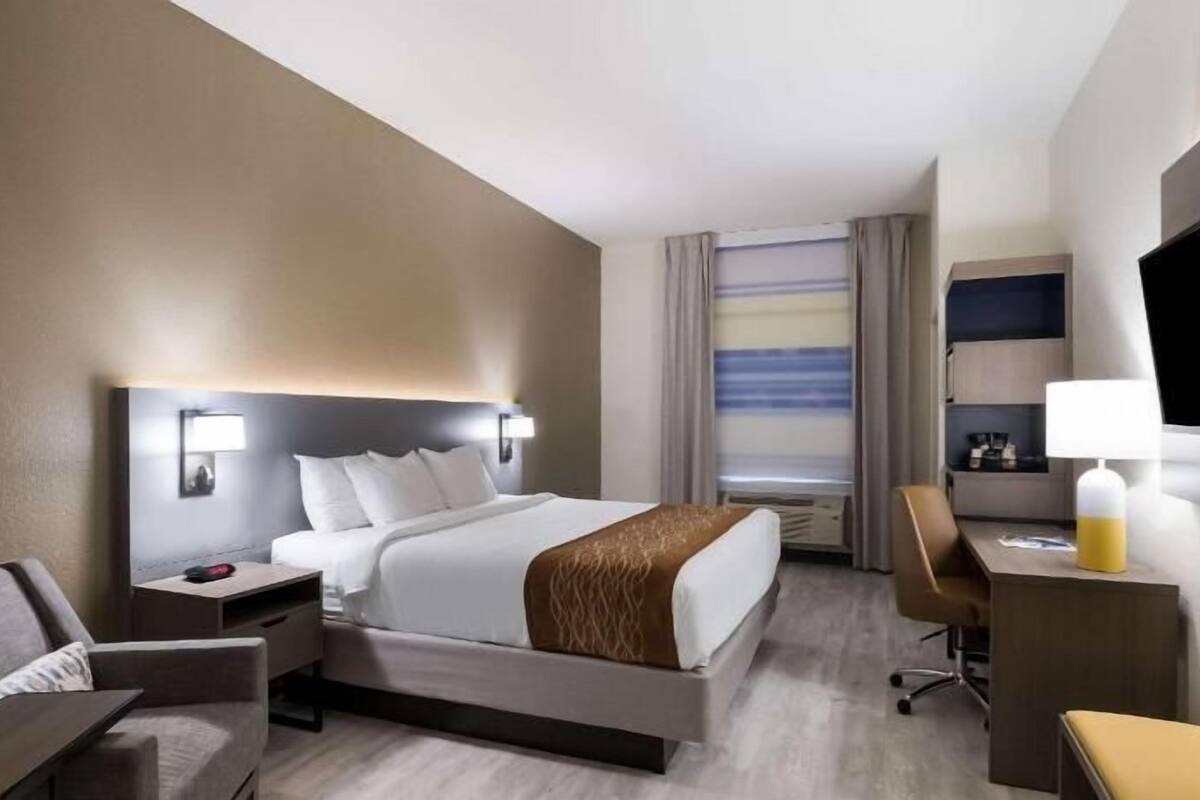 A hotel room with a bed, bedside tables, a desk, a chair, a TV, and a window with curtains.