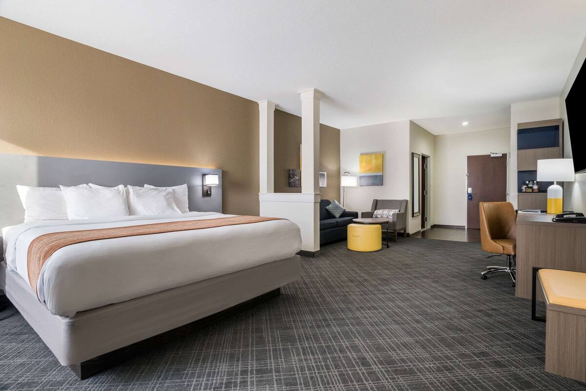 A hotel room with a large bed, a desk with a chair, a sofa, and a small ottoman.