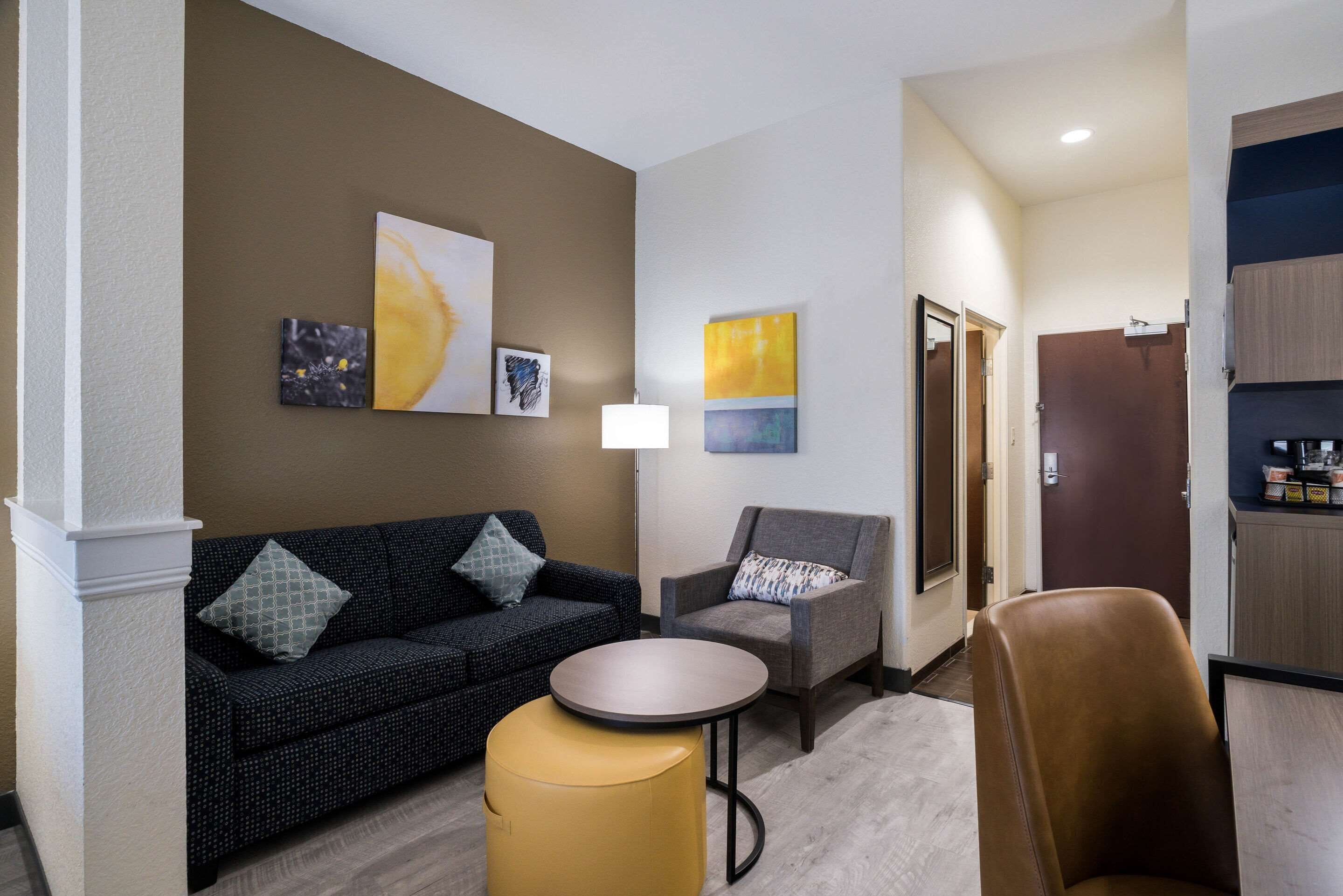Un vestíbulo de hotel con un sofá, un sillón, una pequeña mesa redonda y obras de arte en las paredes.