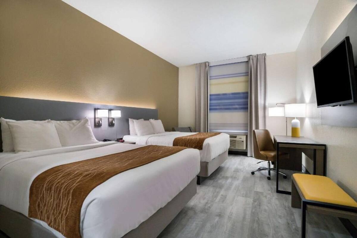 A hotel room with two beds, a desk, a chair, a TV, and a window with curtains.