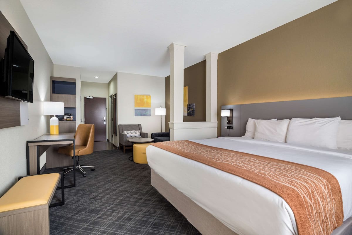 A hotel room with a large bed, a desk, a chair, a small table, and a television.
