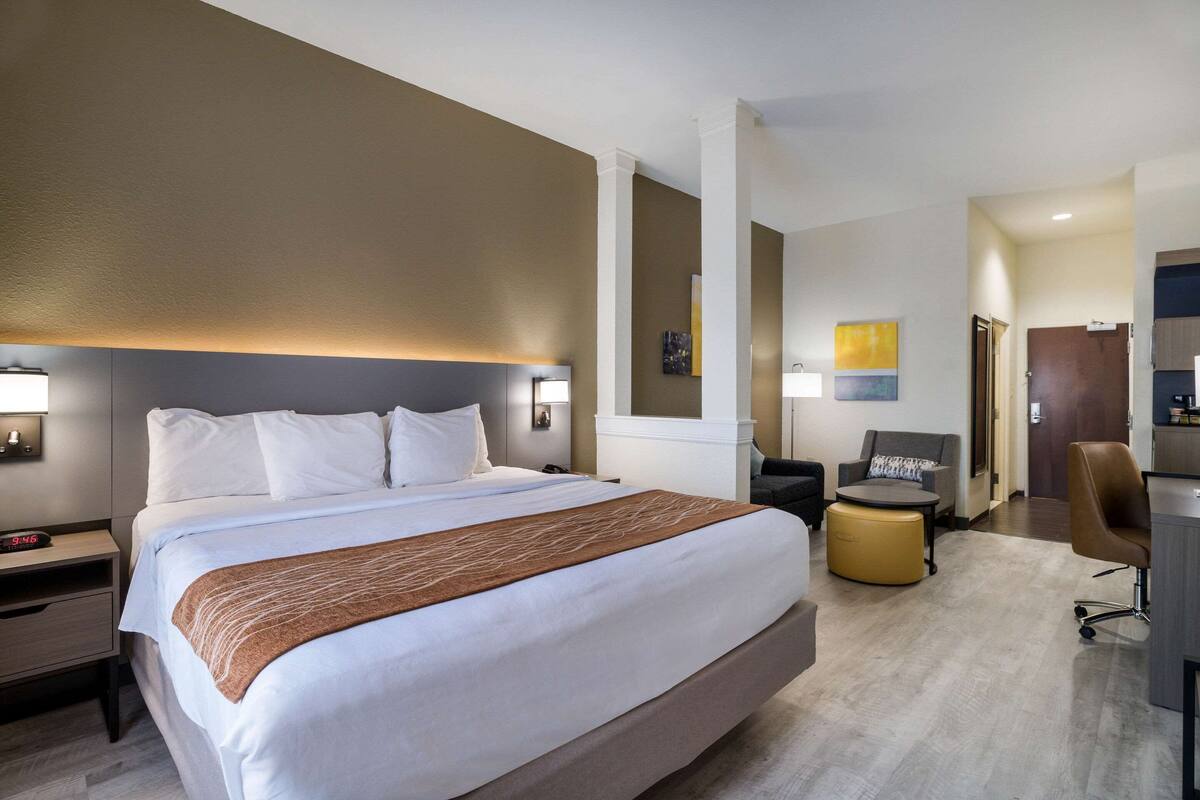 A hotel room with a large bed, bedside tables, a desk, a chair, and a sofa.