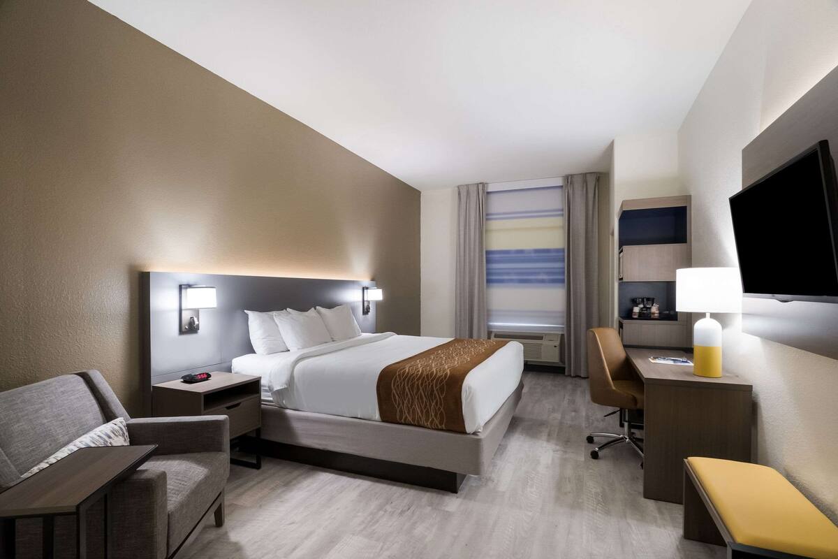 A hotel room with a bed, a desk, a chair, a TV, and a window with curtains.