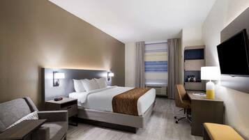 Habitación de hotel con cama, escritorio, silla, televisor y ventana con cortinas.