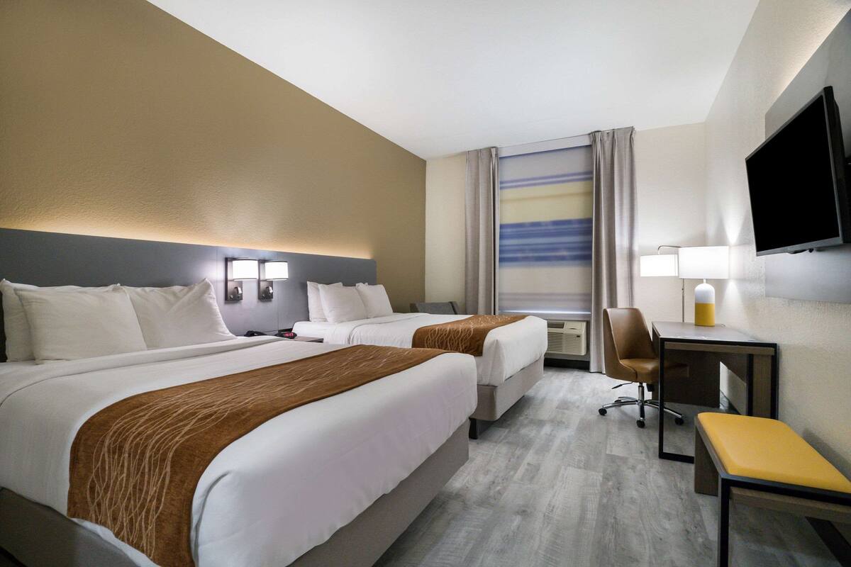 A hotel room with two beds, a desk, a chair, a TV, and a window with curtains.