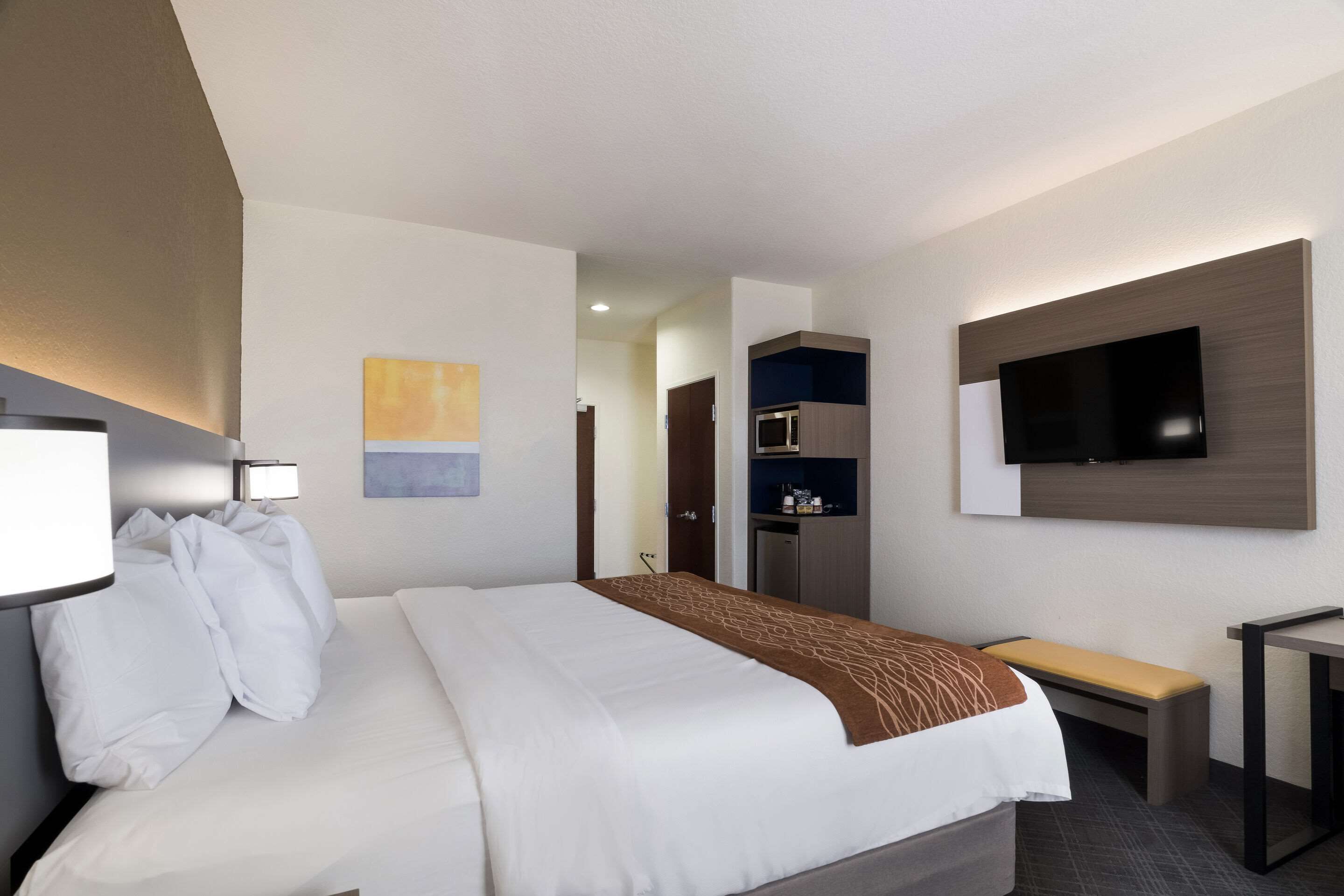 A hotel room with a large bed, a flat-screen TV mounted on the wall, a bedside table, and a small desk.