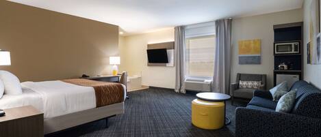 Habitación de hotel con cama, sofá, mesita, televisor, microondas y ventana con cortinas.