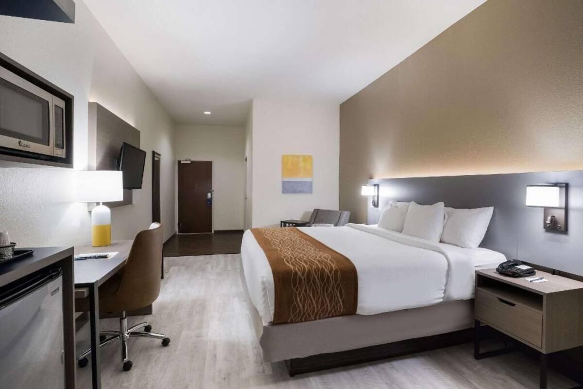 A hotel room with a bed, desk, chair, and a television on the wall.