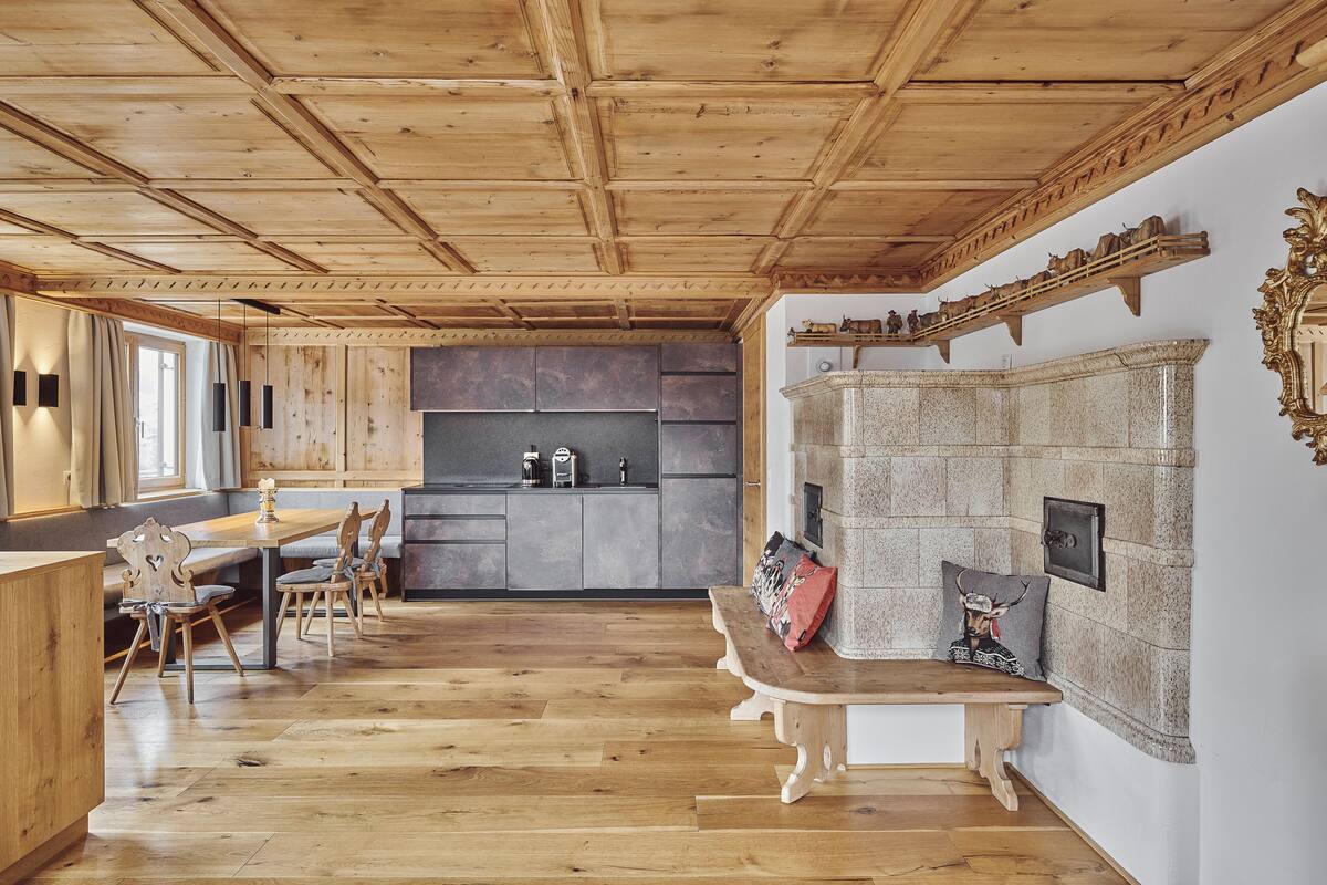 A spacious room with wooden flooring, a wooden ceiling, a built-in kitchen area, a seating area with a bench, and a decorative wall with a mirror and shelf.