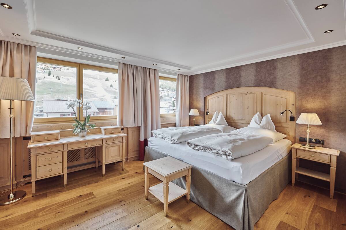 A hotel room with a large bed, wooden furniture, a desk, and a view of a snowy landscape through the window.
