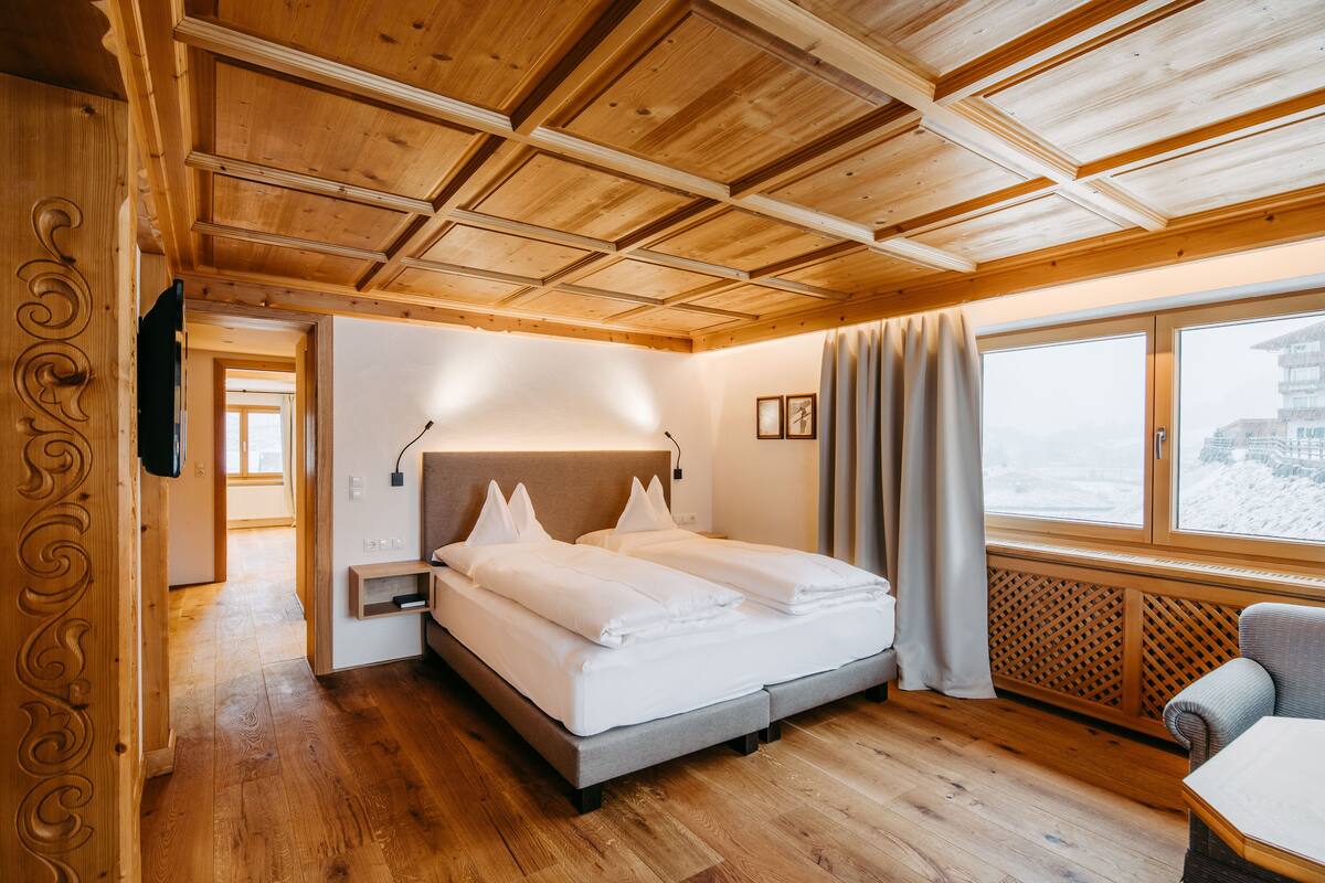 A wooden-paneled room with a bed, a chair, and a window with a view of a snowy landscape.