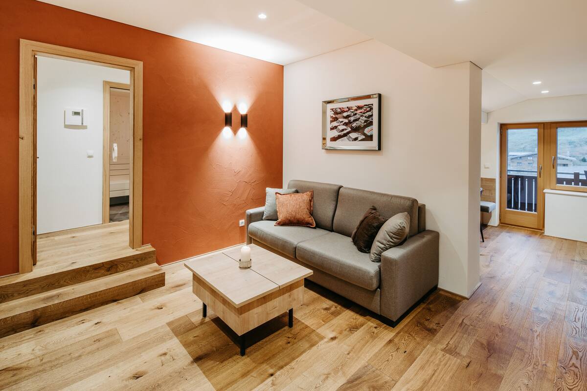 A modern living room with a grey sofa, wooden coffee table, and orange walls.