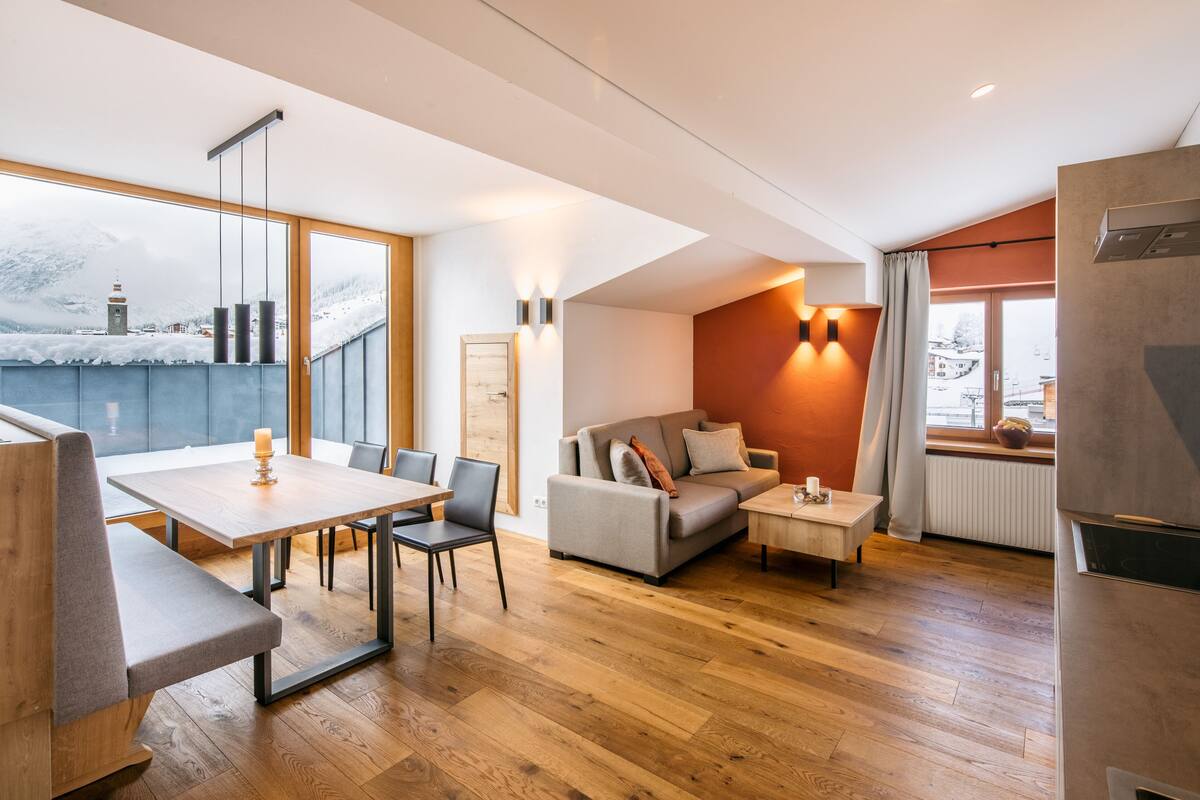 A modern living room with a dining area, large windows, and a view of a snowy landscape.