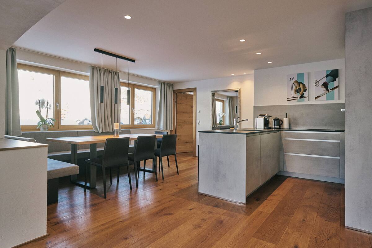 A modern kitchen with wooden flooring, a dining area with a bench, and a large window with curtains.