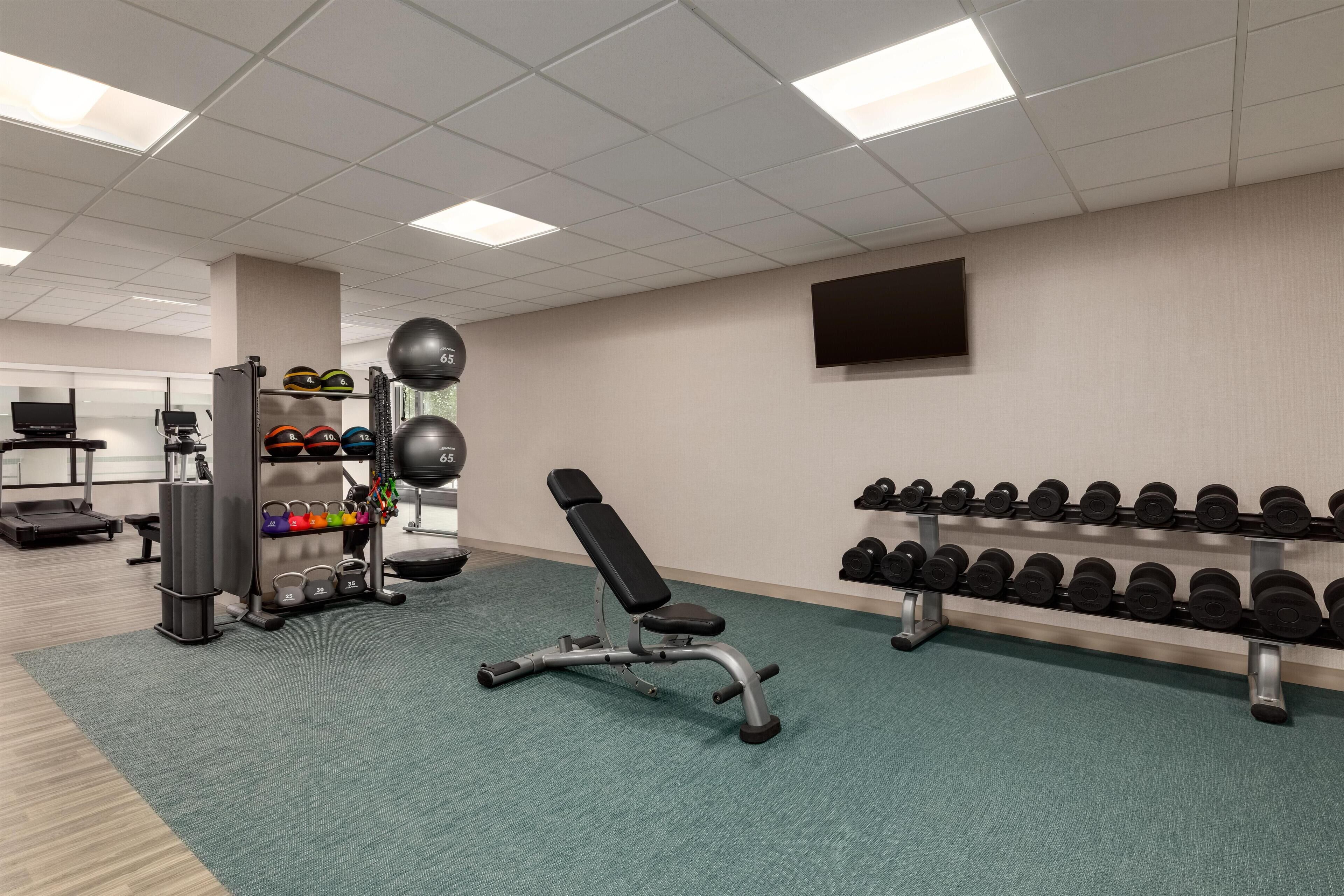 Ein Fitnessraum mit Trainingsgeräten, Kurzhanteln und Laufband.