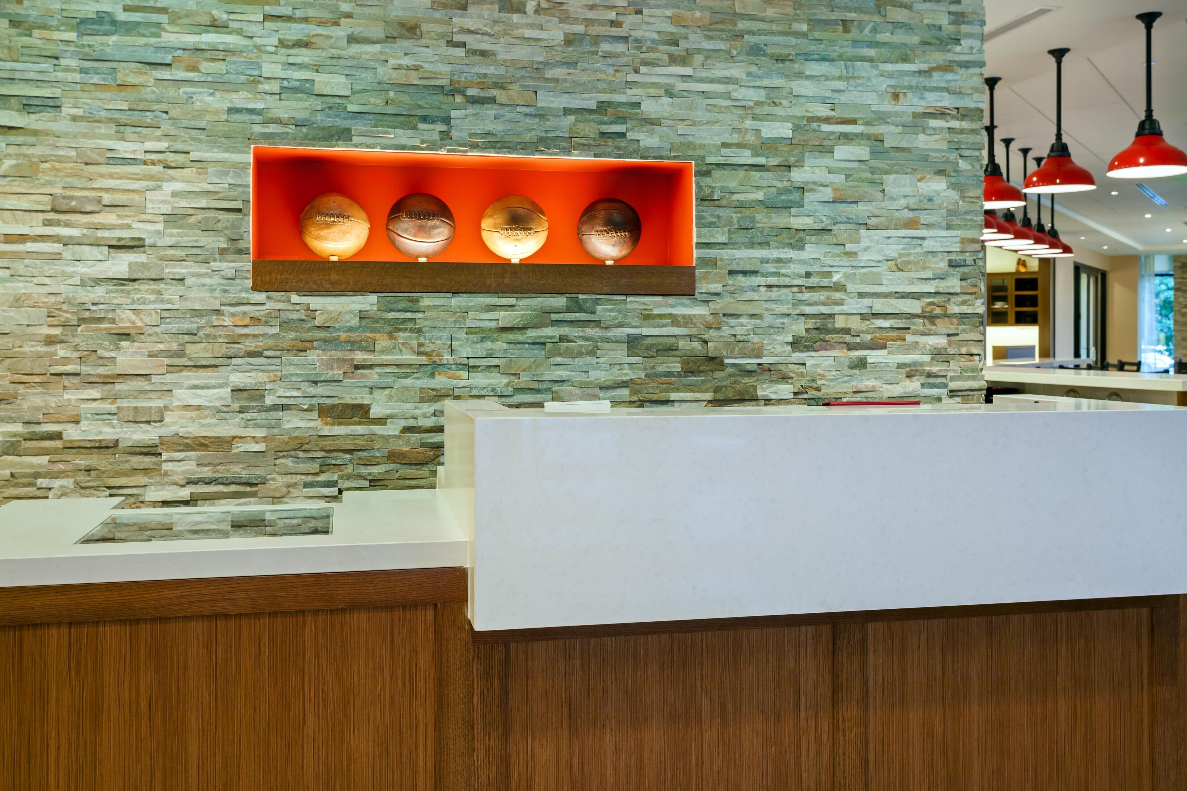 A reception area with a stone wall, a wooden reception desk, and a red shelf with three illuminated objects.