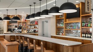 A bar area with multiple seating options, a variety of liquor bottles, and a sign reading "THE PLAGERY". - Hyatt Place Bloomington (Bloomington)
