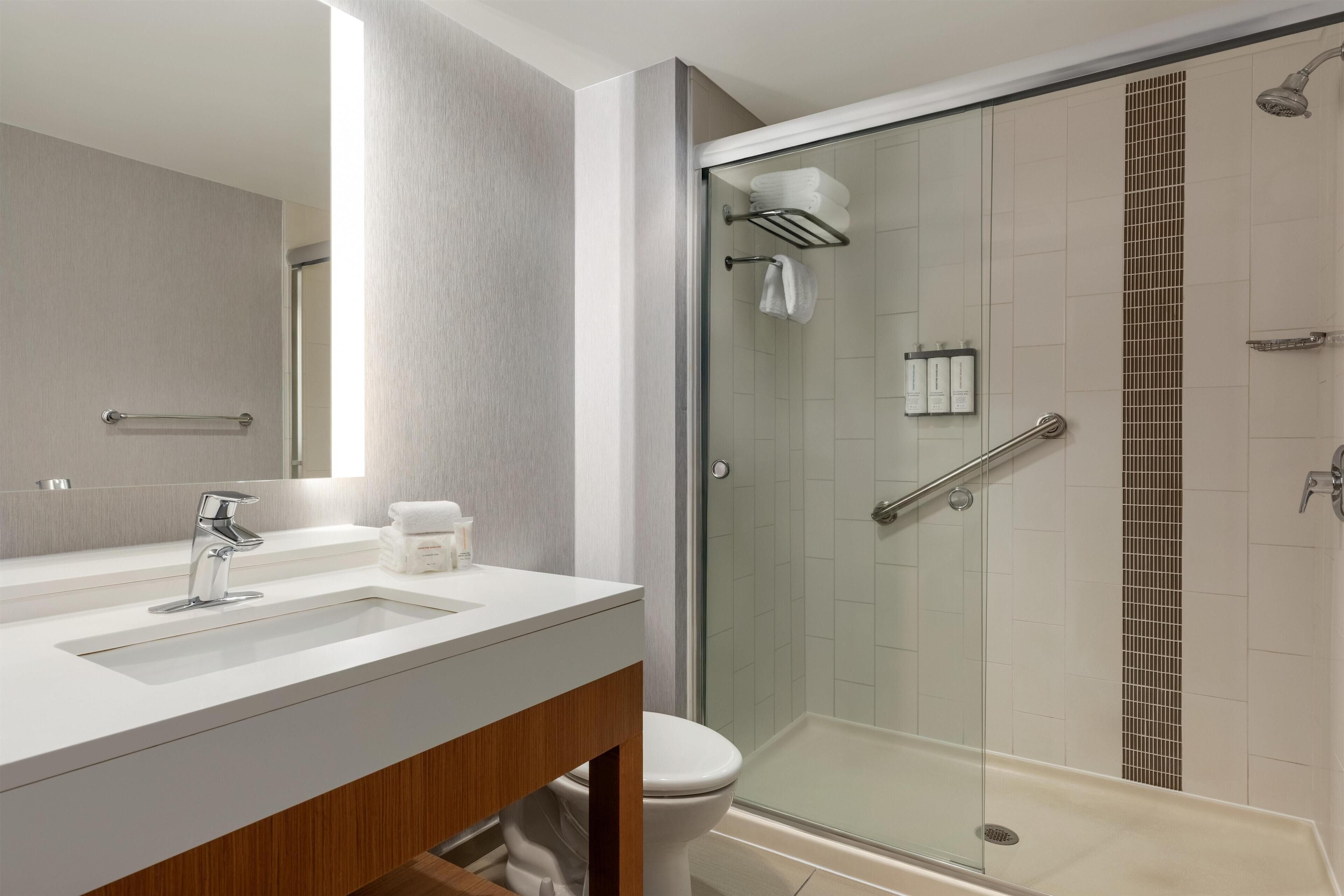 Un baño moderno con ducha de vidrio, lavamanos blanco y tocador de madera.