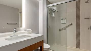Un baño moderno con ducha de vidrio, lavamanos blanco y tocador de madera.