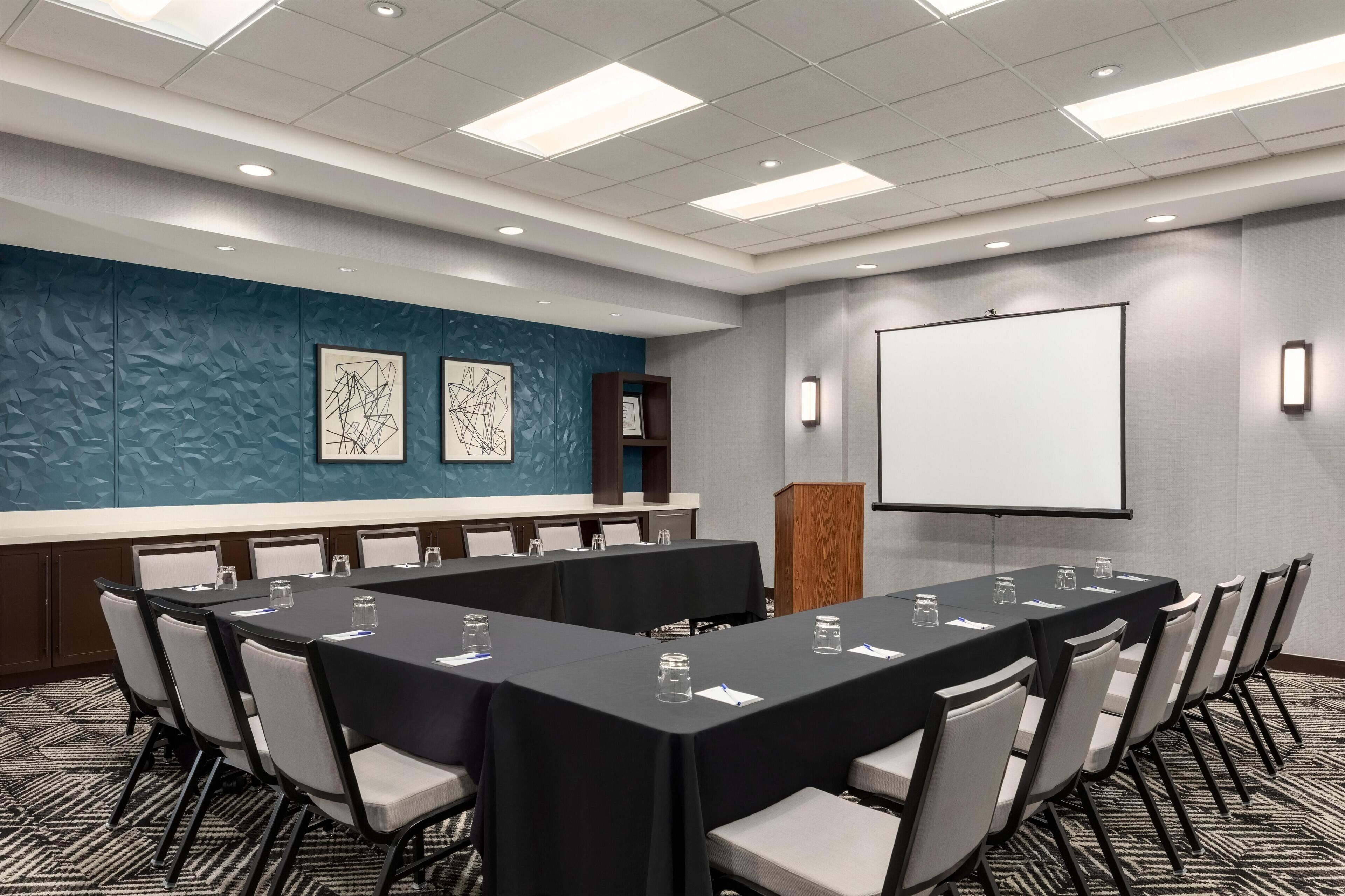 A conference room with a long table, chairs, a projector screen, and a whiteboard.