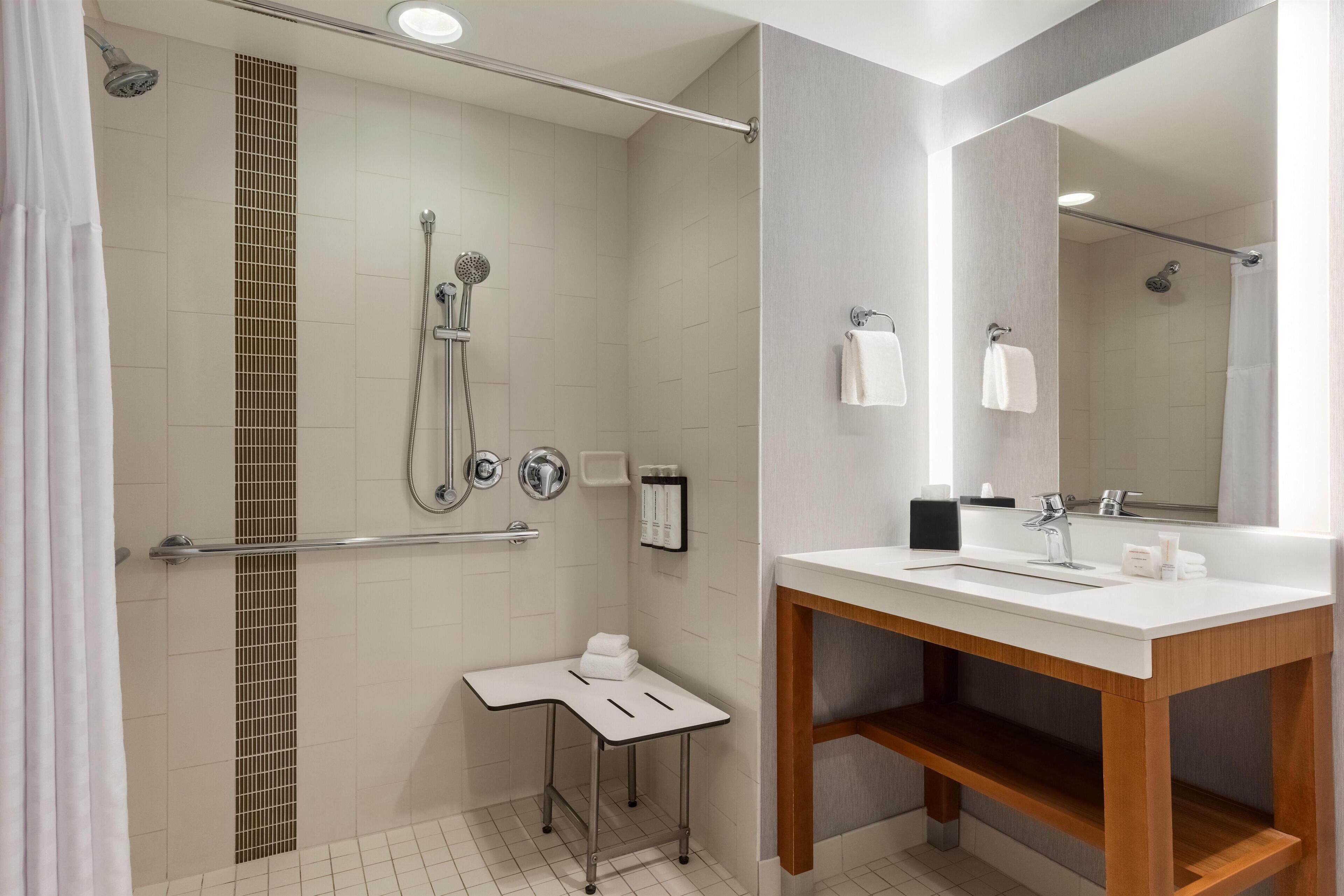 A modern bathroom with a shower, a sink, a mirror, and a small table with towels.