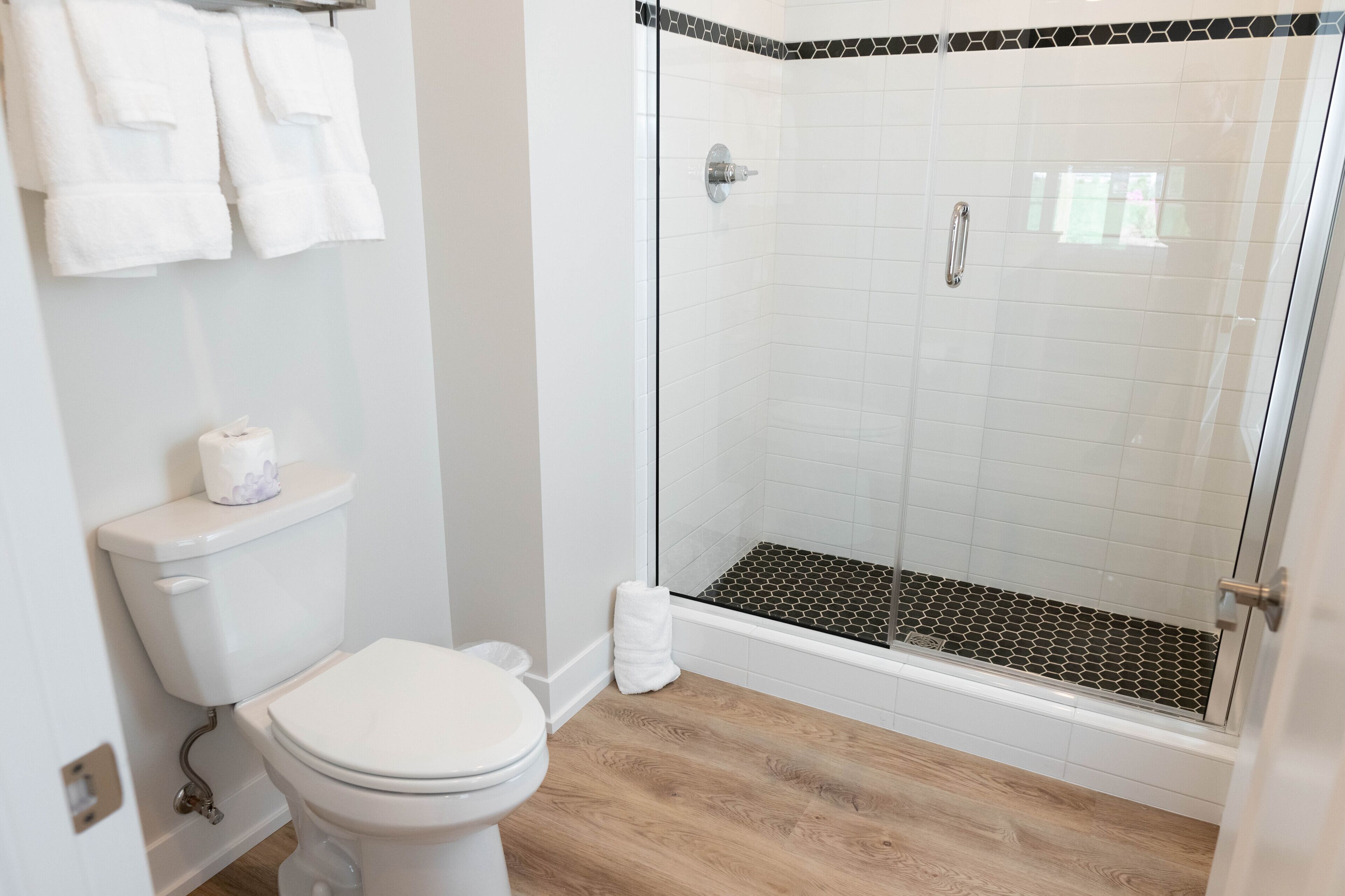 A bathroom with a toilet, a glass-enclosed shower with a black and white tiled floor, and a white towel rack.