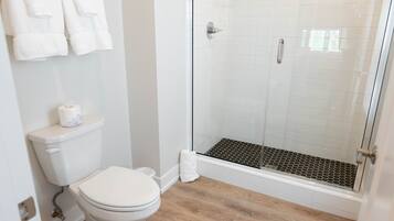 A bathroom with a toilet, a glass-enclosed shower with a black and white tiled floor, and a white towel rack.