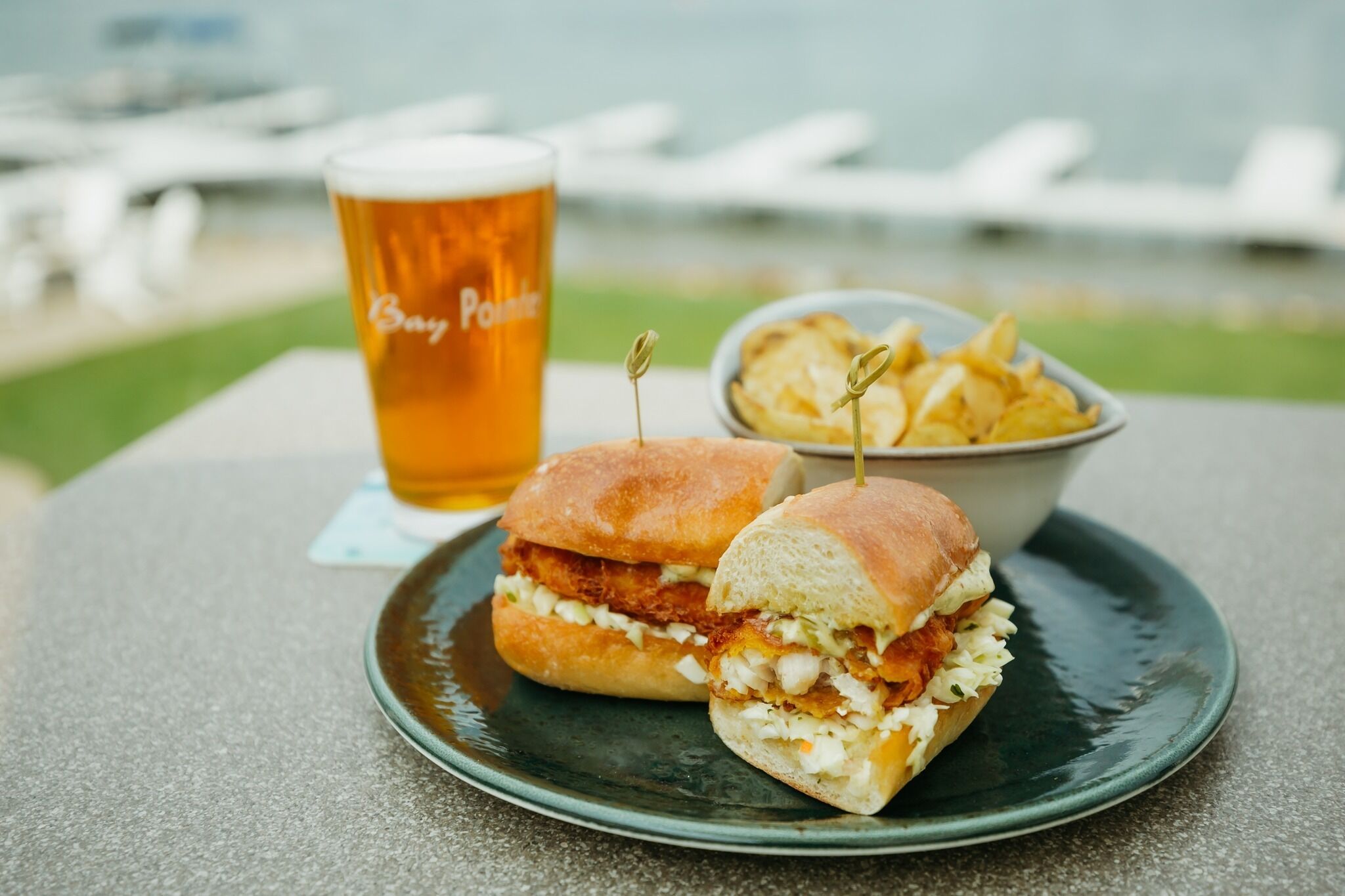 Un panino con patatine fritte e una birra in un bicchiere su un tavolo con vista sull'acqua.