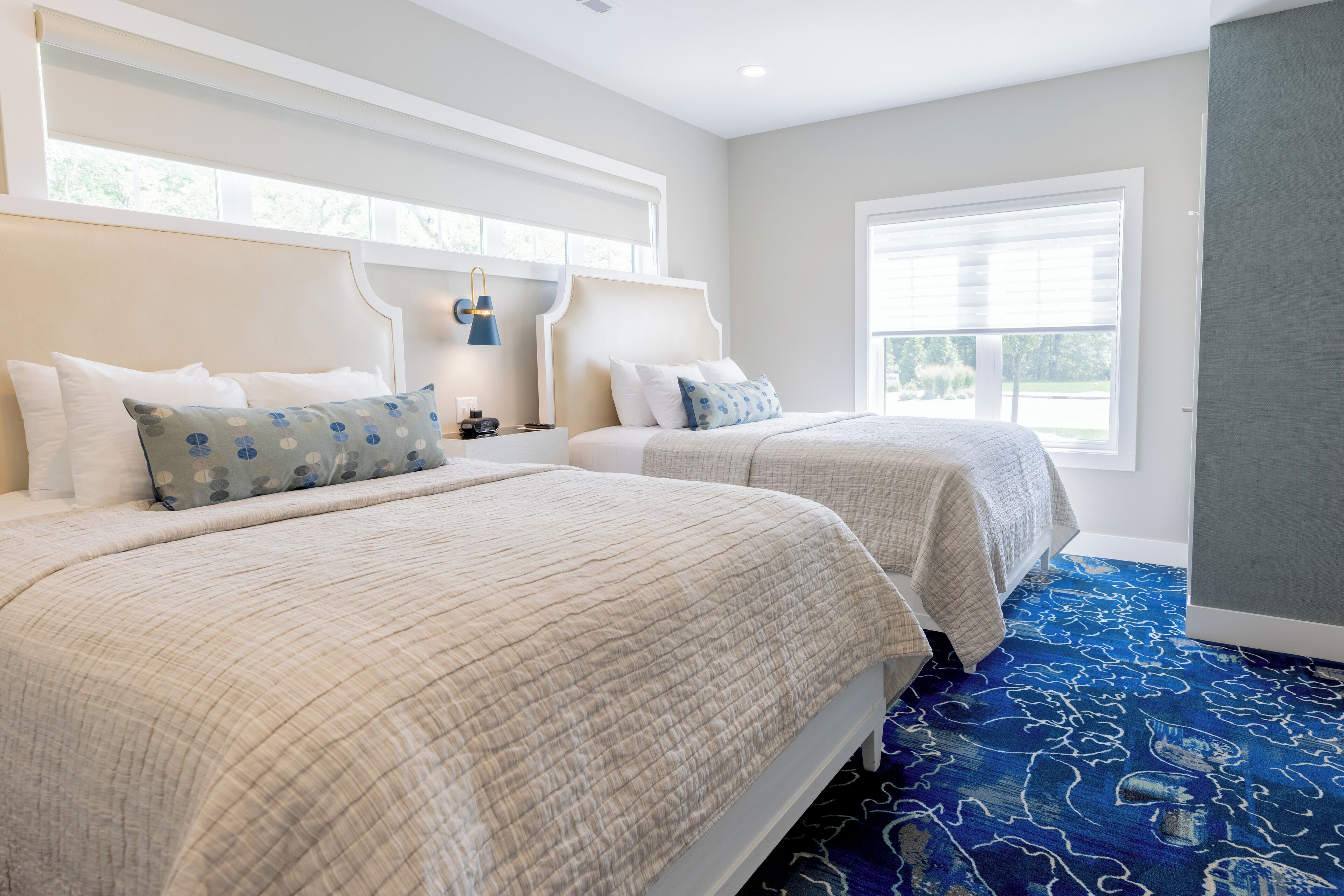 A hotel room with two beds, a large window, and a blue patterned carpet.