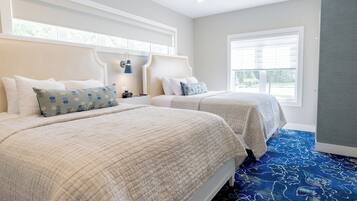 A hotel room with two beds, a large window, and a blue patterned carpet.