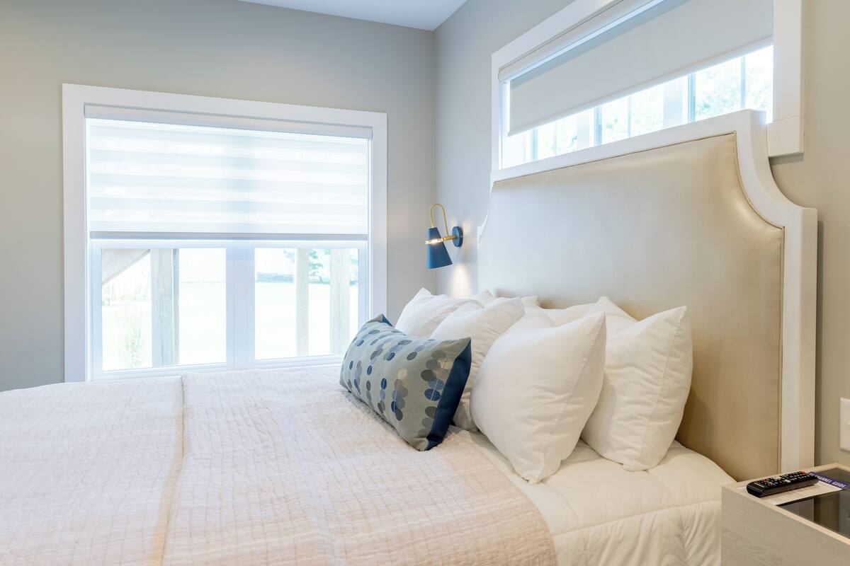 A bedroom with a large bed, a nightstand, a wall-mounted lamp, and a window with blinds.