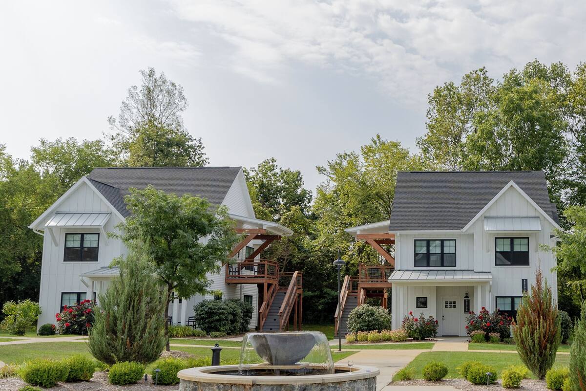 A modern two-story house with a stone fire pit in the front yard, surrounded by well-maintained landscaping and trees.
