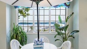 Un espace repas comprenant une table et des chaises, avec vue sur un lac et agrémenté de grandes plantes en pot.
