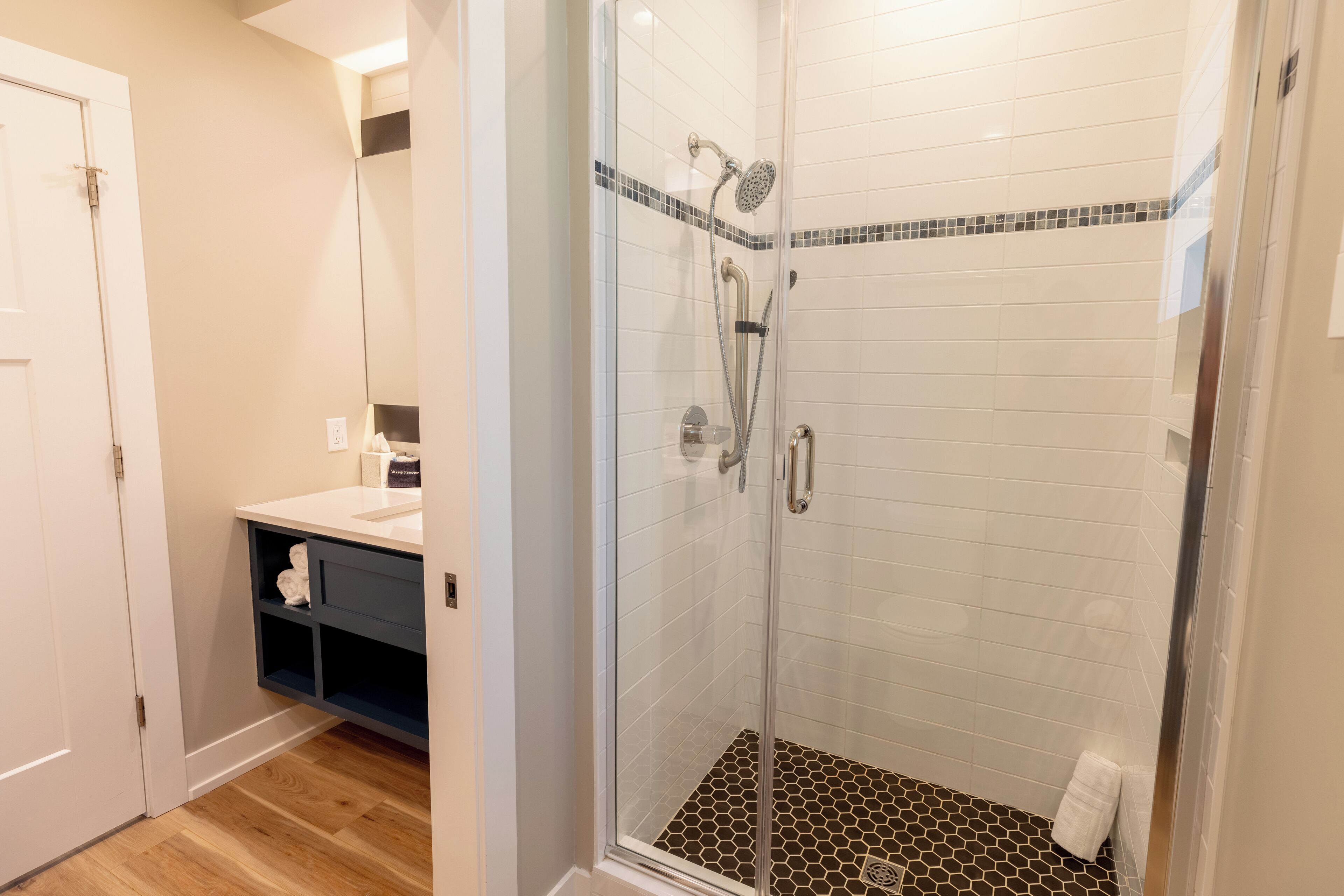 A glass-enclosed shower with a tiled floor, a white sink with a dark cabinet, and a mirror above the sink.