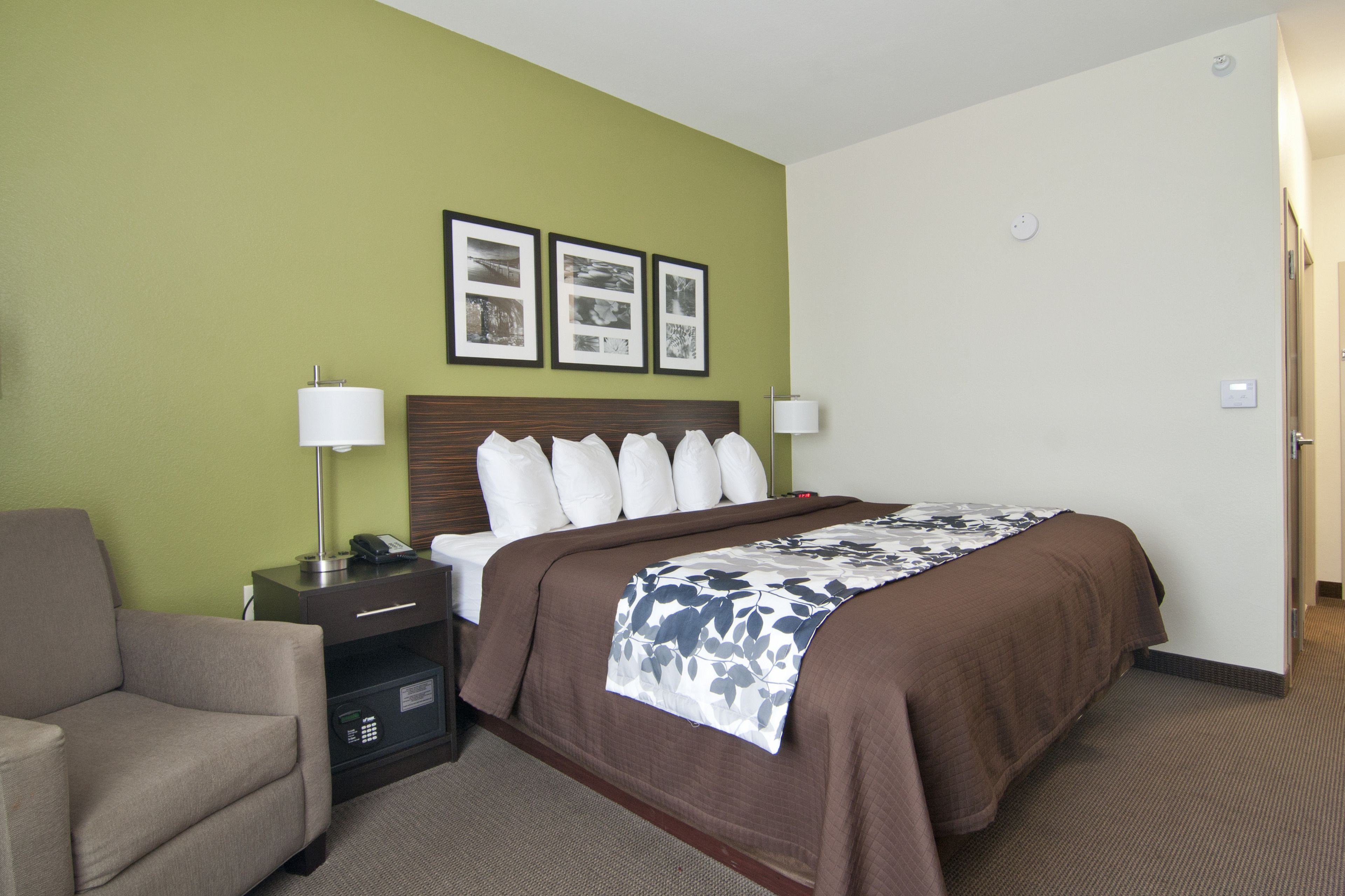 A hotel room with a bed, a chair, a desk, and a nightstand. There are three framed pictures on the wall above the bed.