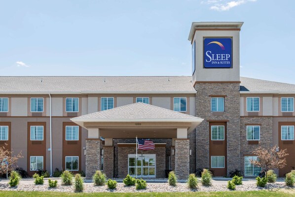 Edificio Sleep Inn & Suites con fachada de piedra, varias ventanas y una bandera estadounidense.