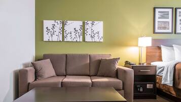 Ein Hotelzimmer mit Sofa, Nachttisch, Lampe, Bett und Kunstwerk an der Wand.
