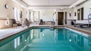 Una piscina interior con agua cristalina, rodeada de sillones de descanso y una zona de estar cubierta.